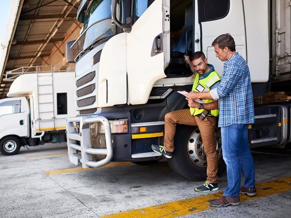 Shot of two coworkers talking together next to a large truck outside of a distribution center
